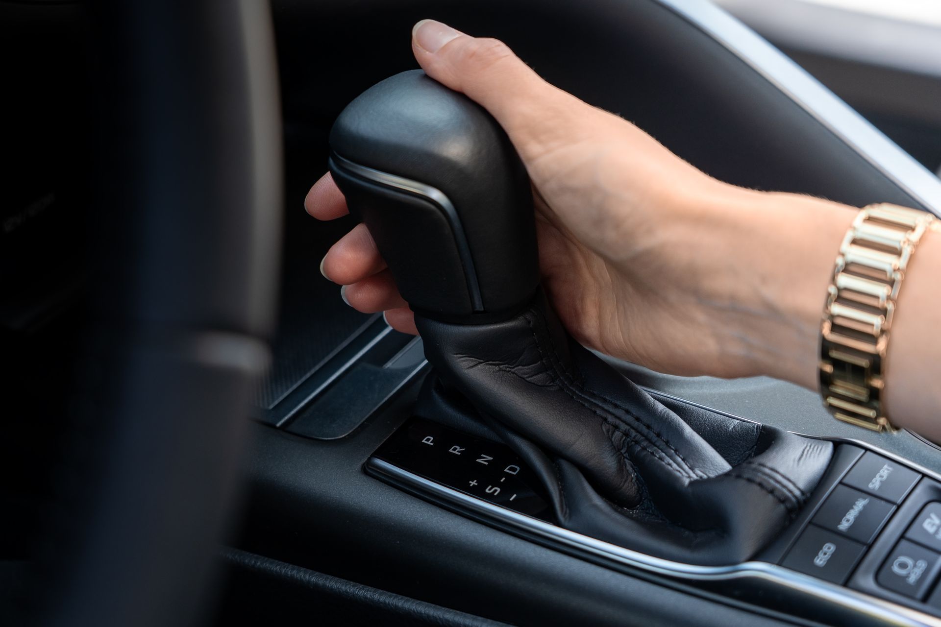 Woman’s hand on auto gear shift showing PRND and drive modes in modern car interior. Woman’s hand on auto gear shift showing PRND and drive modes in modern car interior.