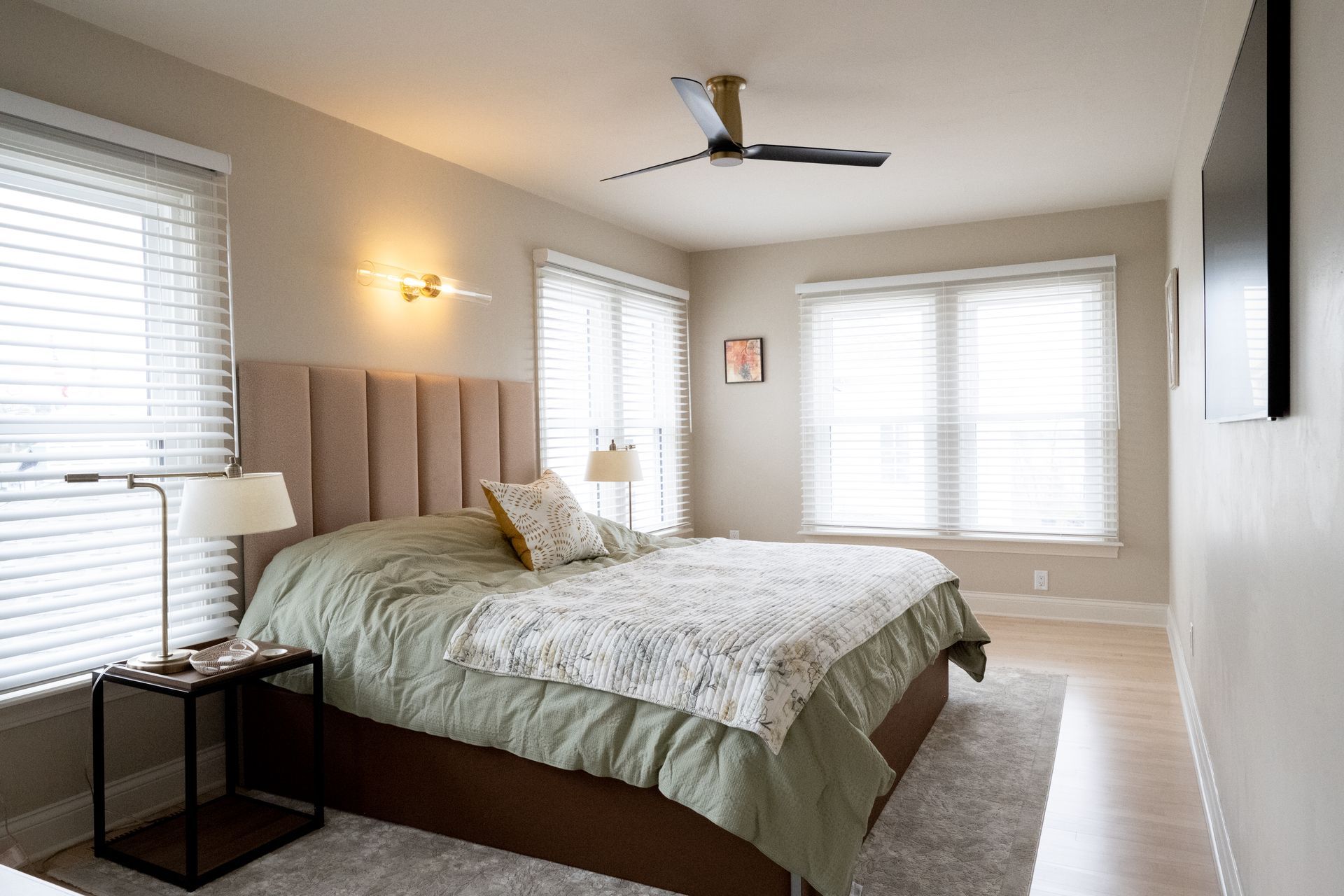 A bedroom with a bed , dresser , nightstand , rug and two windows.