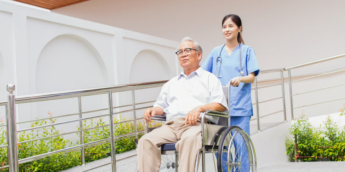 Nurse pushing a person in a wheelchair up a ramp outside a building.