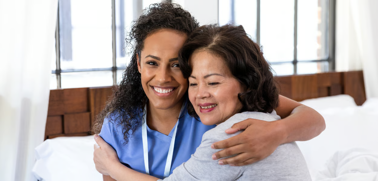 Two people smiling, hugging. One wears blue scrubs.