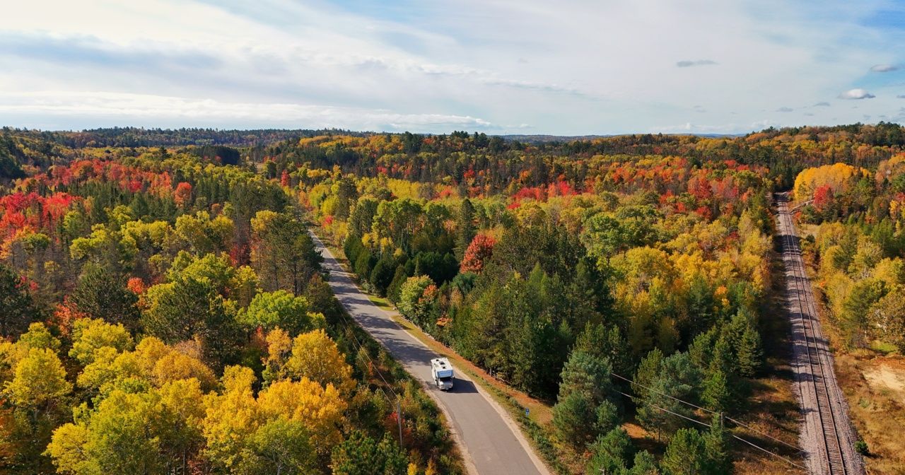 An aerial view of a car driving down a road surrounded by trees in the fall.