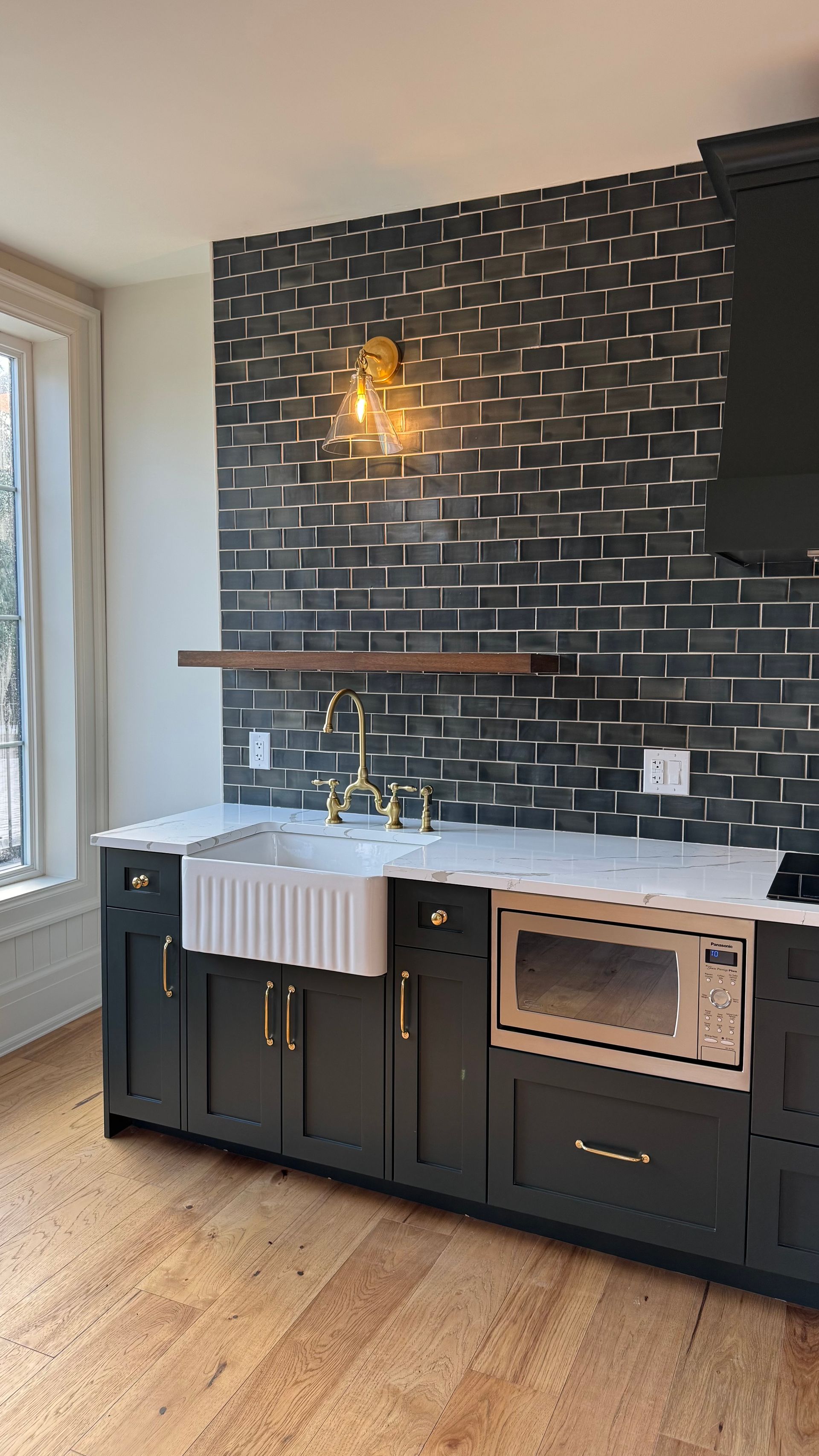 A kitchen with black cabinets , a sink , a microwave , and a window.