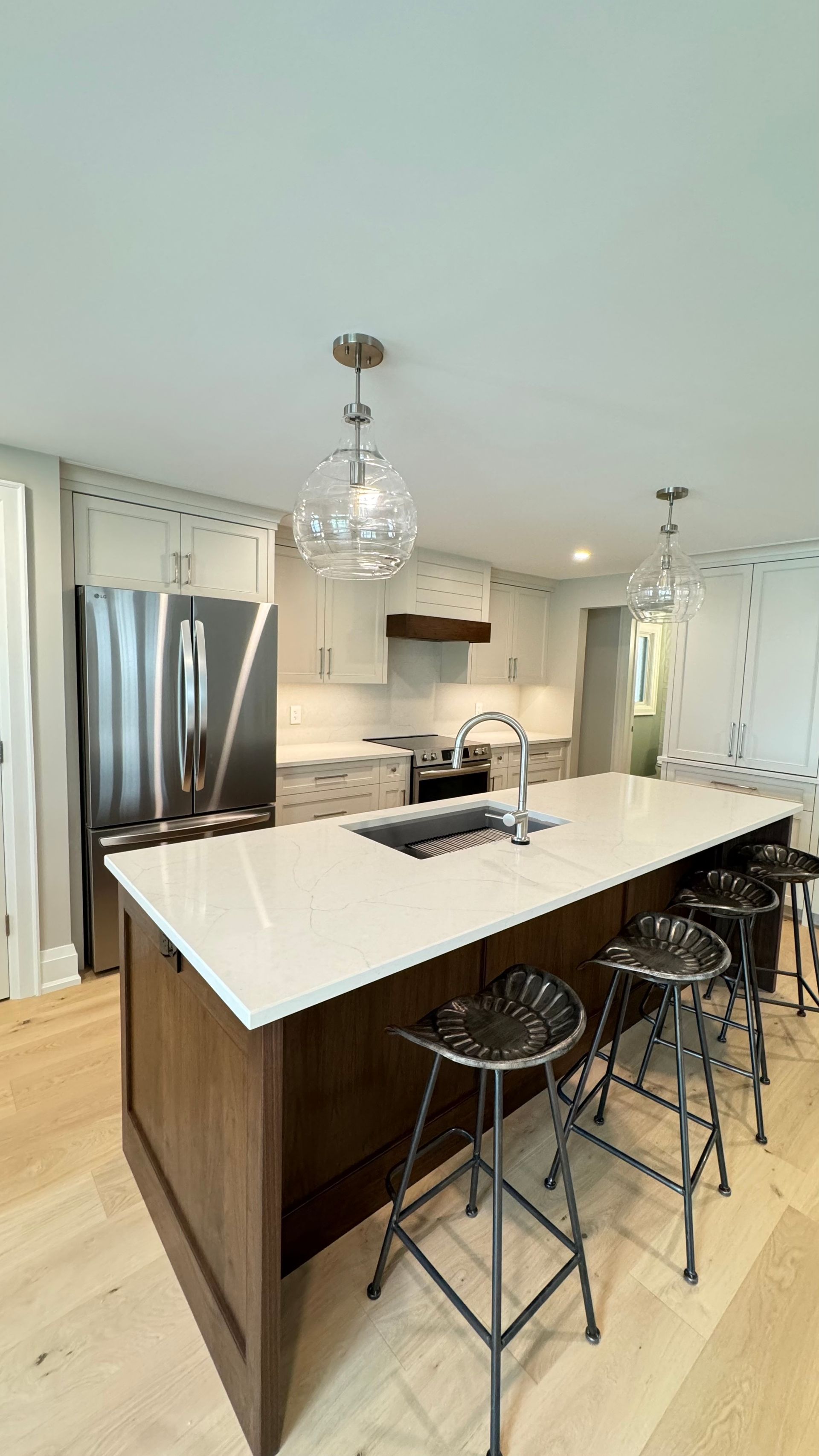 A kitchen with a large island , sink , refrigerator and stools.