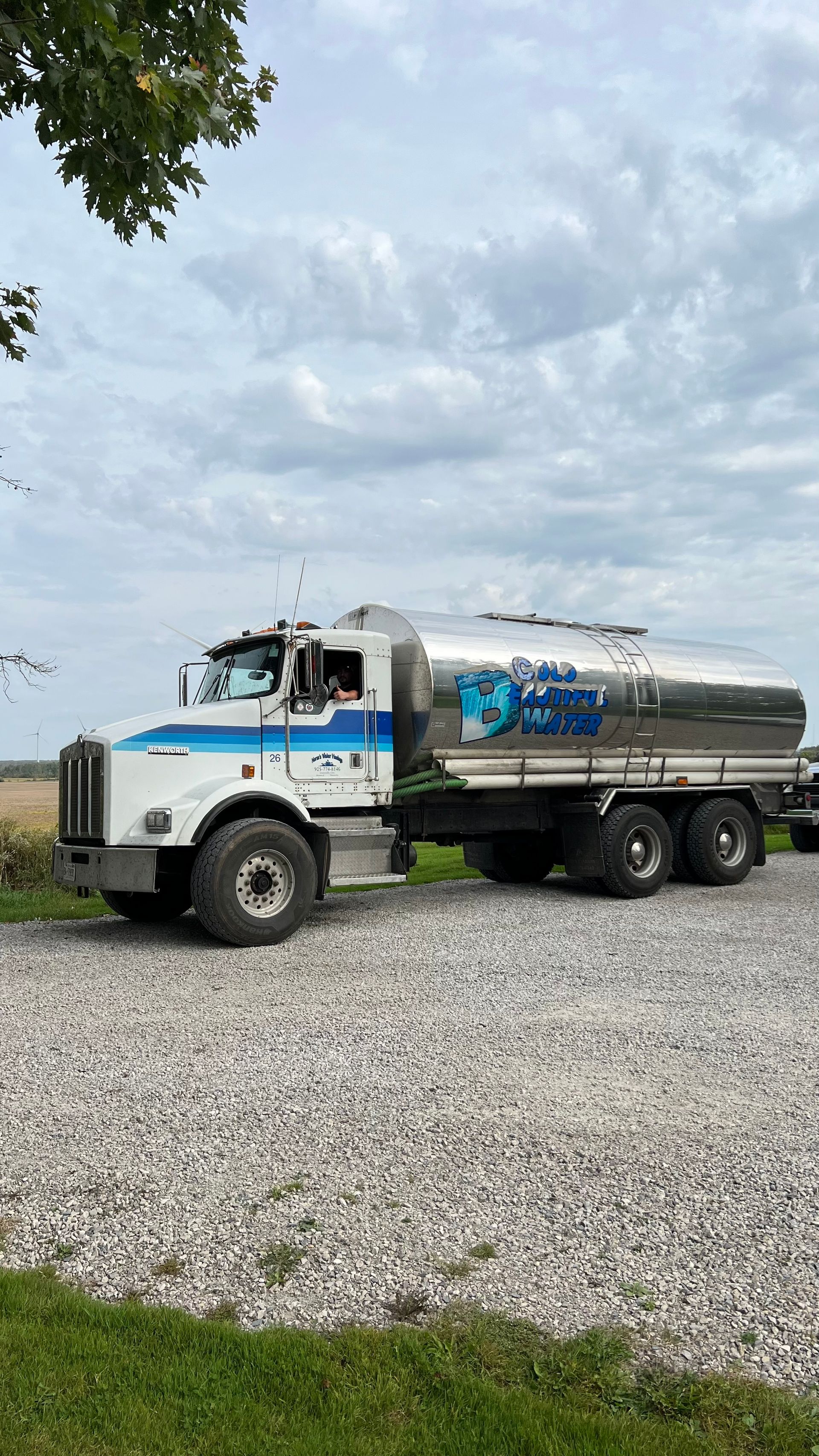 A white and blue tanker truck is parked in a gravel lot.