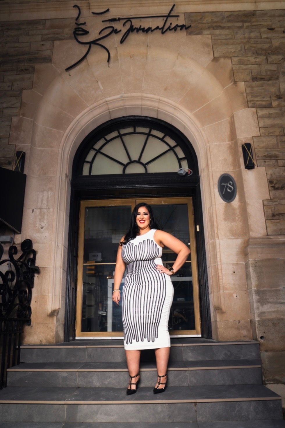 A woman in a black and white dress is standing in front of a building.