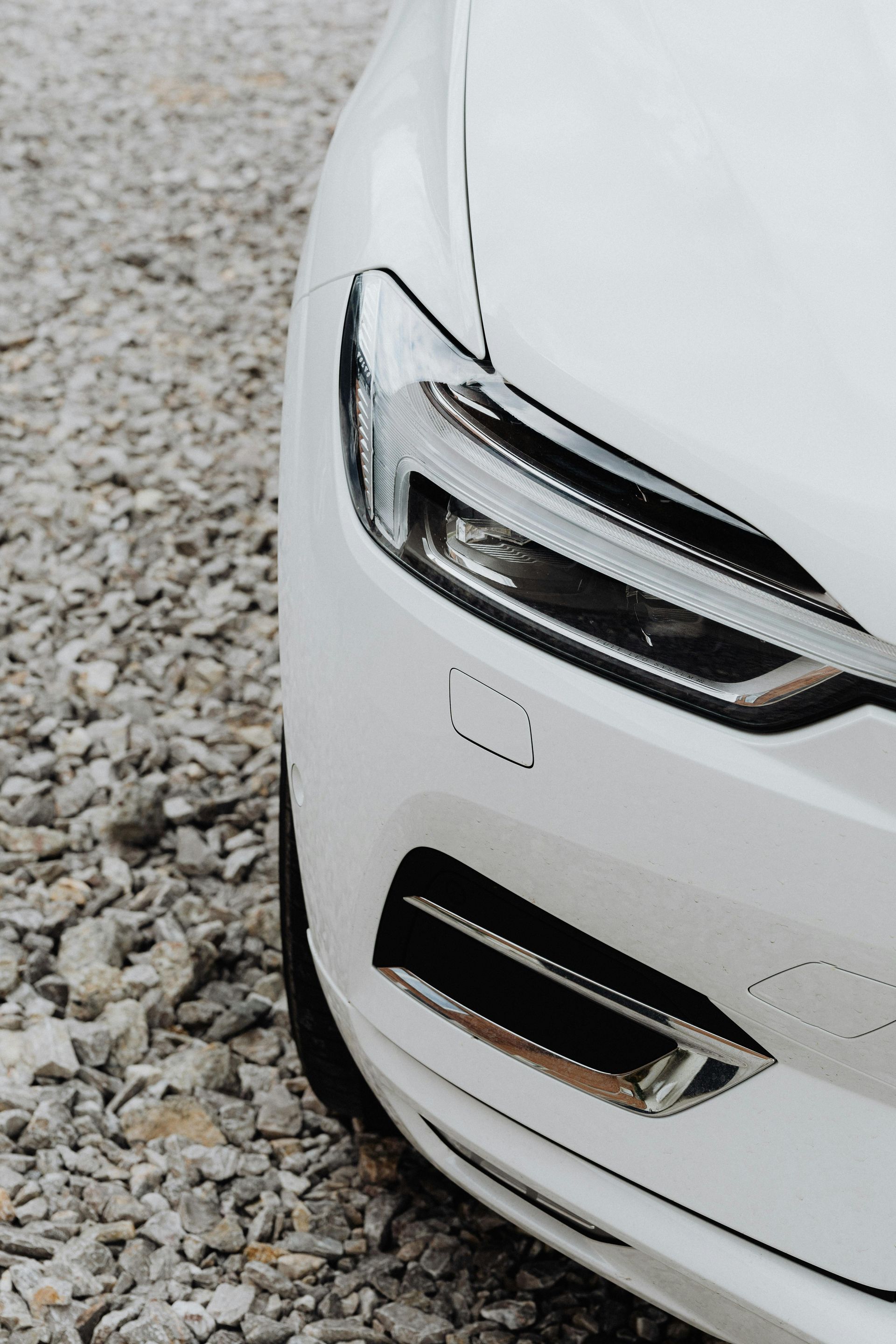 White car's front corner with headlight and fog light on gravel.