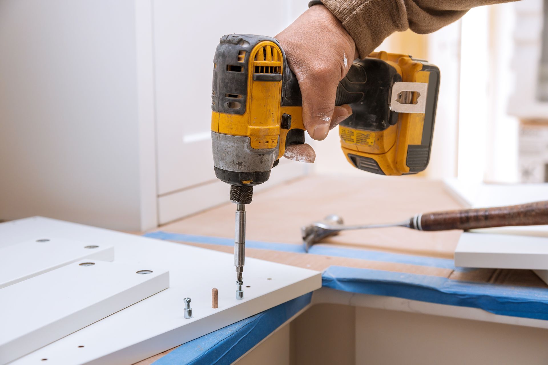 Hand holding a yellow drill assembling white furniture in a bright room