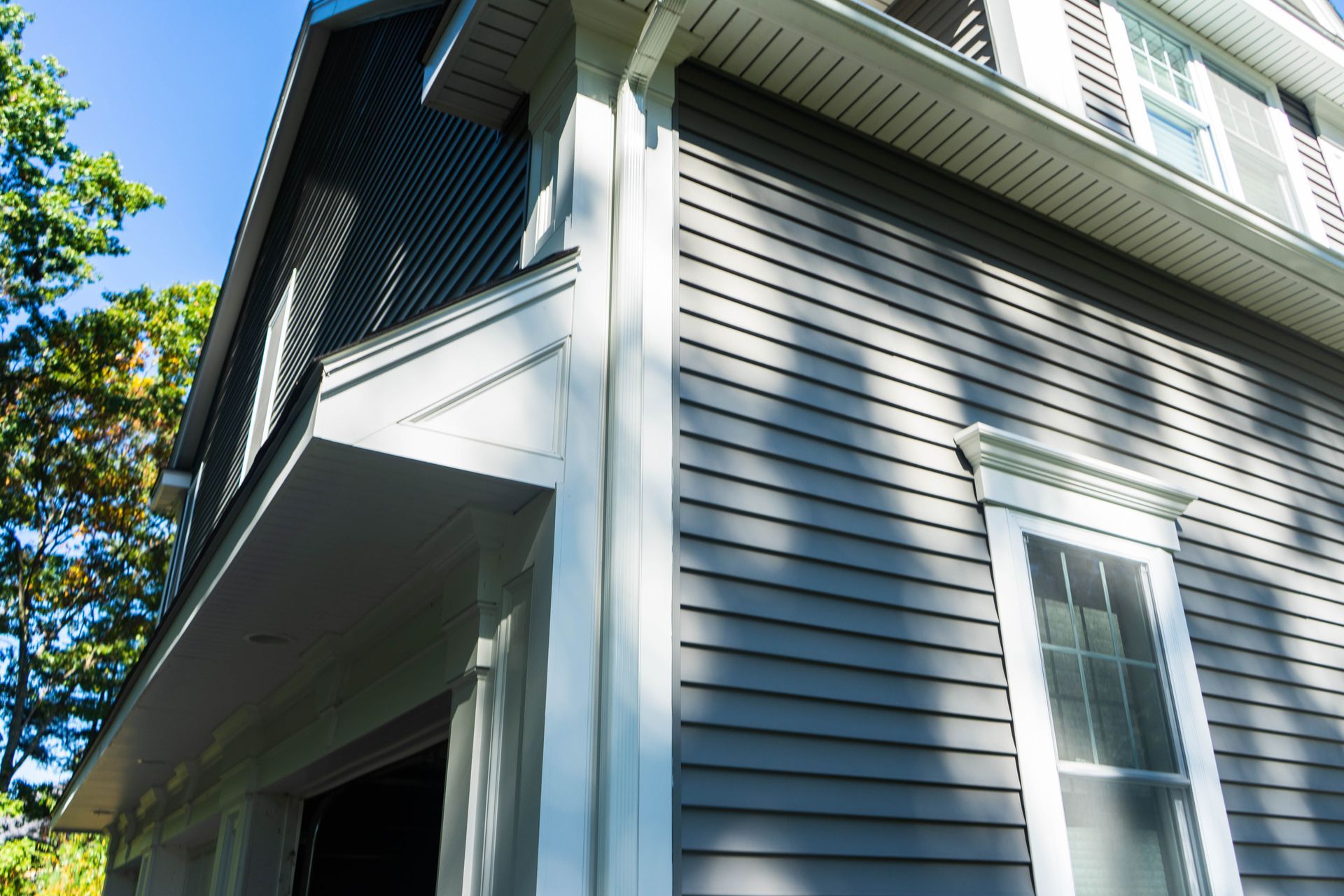 Gray house exterior with white trim and porch roof under a blue sky