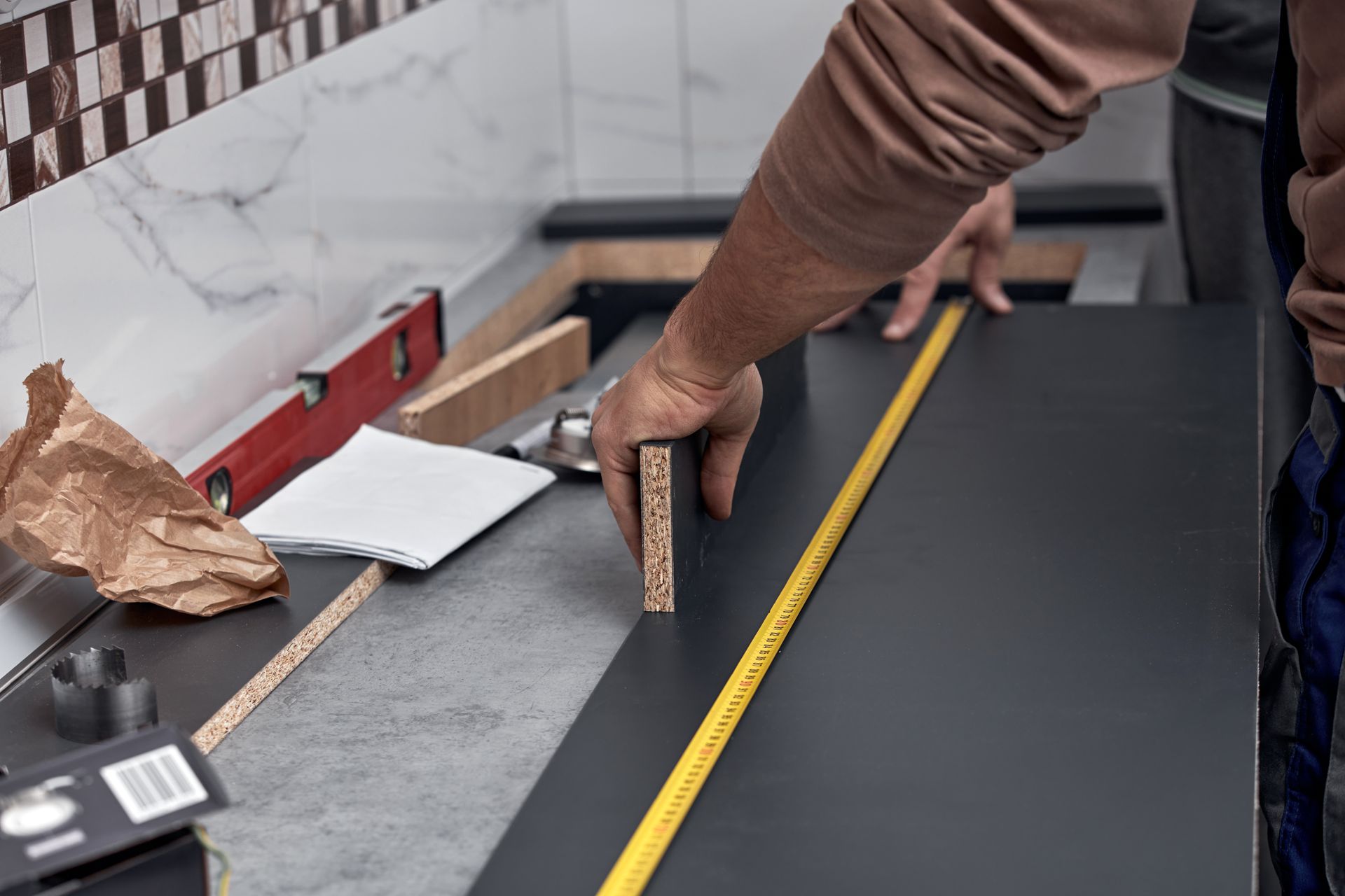Hand measuring a dark countertop with a yellow tape measure in a kitchen under renovation