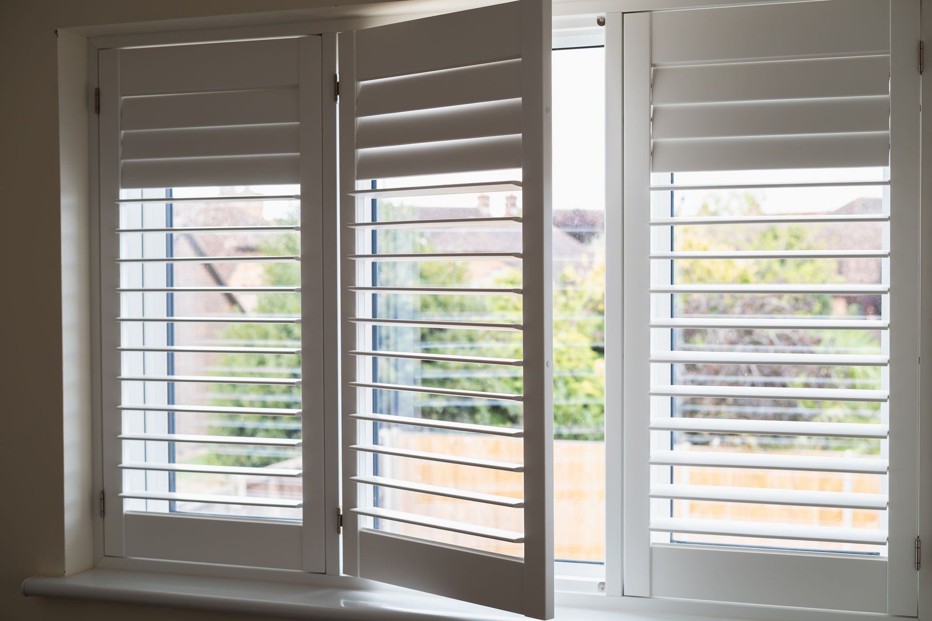 White window shutters with slats open to a bright view outside.