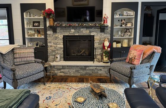 Living room fireplace with built-in shelves, patterned chairs, and a large TV above the mantel
