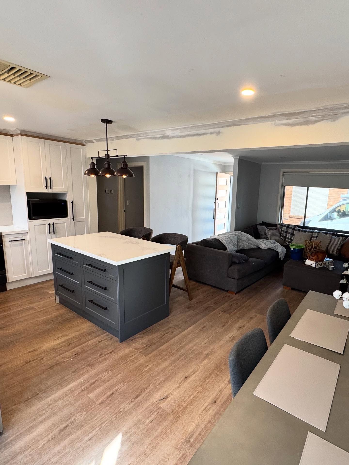 Open-plan kitchen and living room with dark gray sofas, white cabinets, and an island.