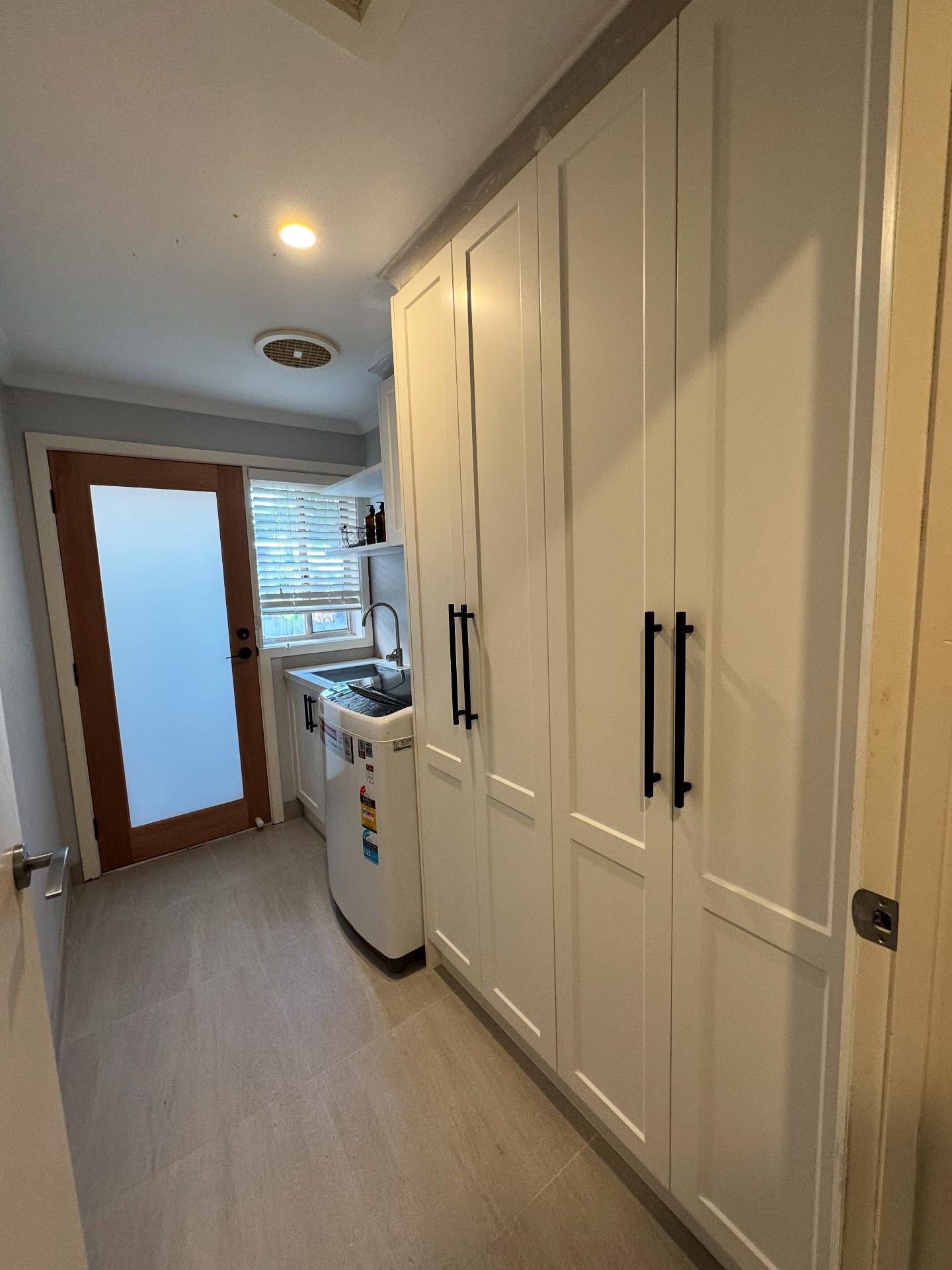 Narrow kitchen hallway with white cabinets, washer, sink, and wood-framed door at the end.