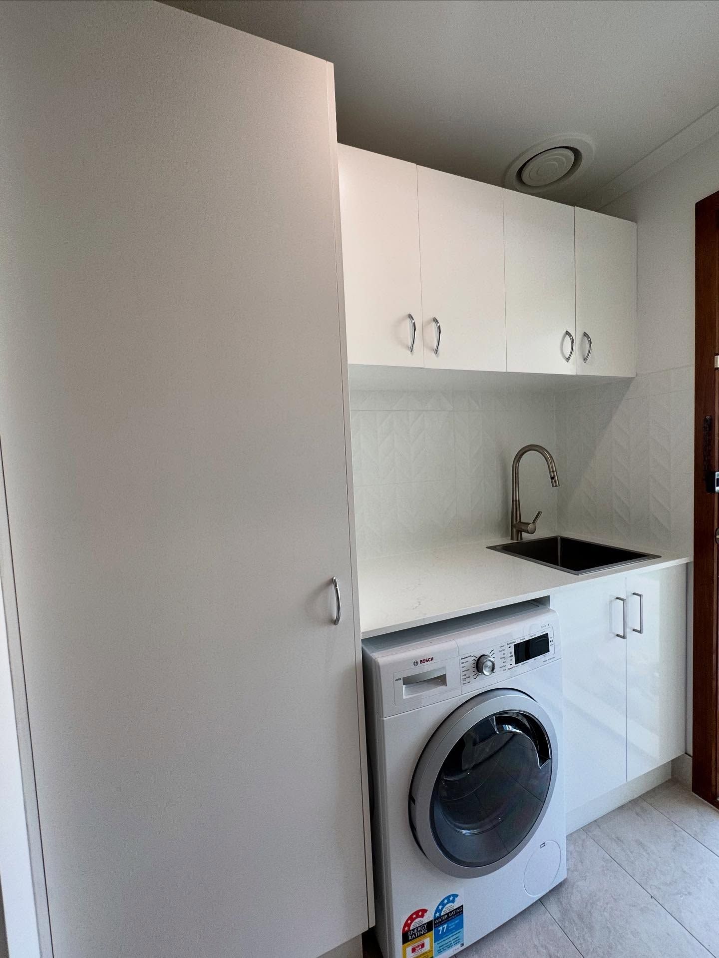 Compact laundry nook with white cabinets, sink, and front-loading washer in a small hallway.