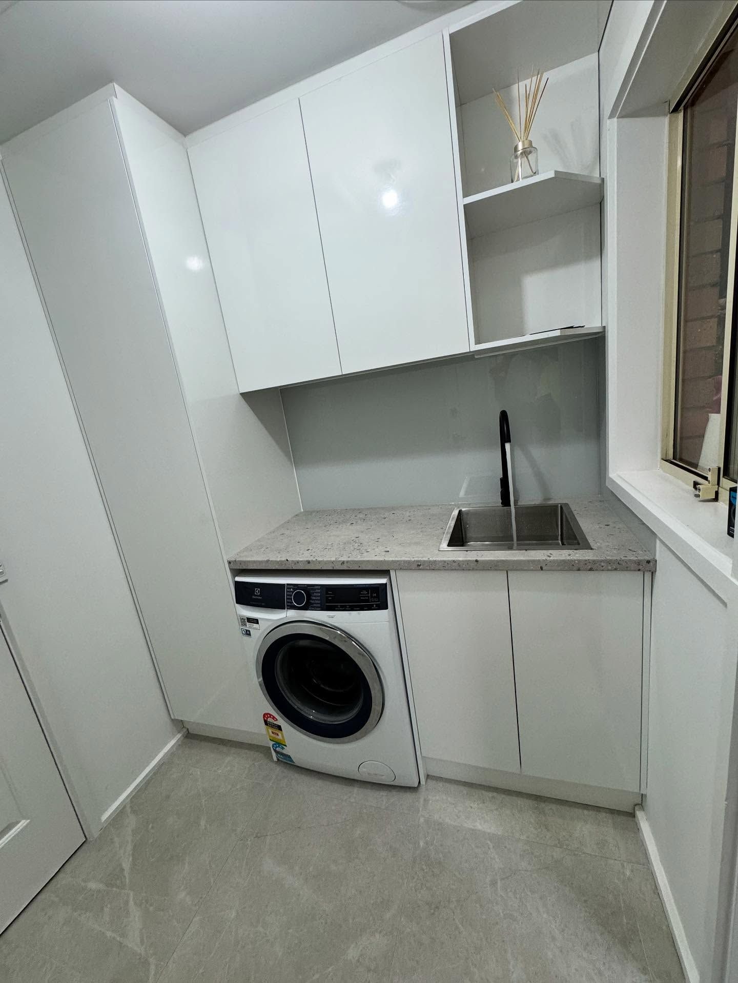 Compact laundry room with white cabinets, front-load washer, sink, countertop, and tiled floor.