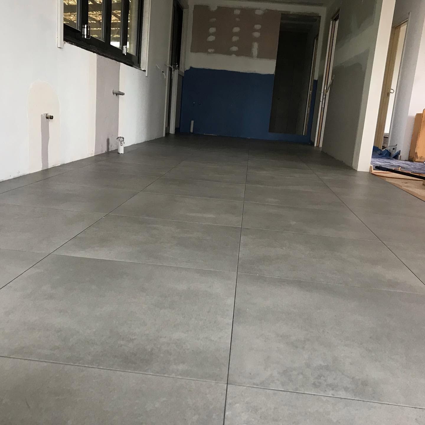 Empty corridor with large gray floor tiles, white walls, and blue door at the end.