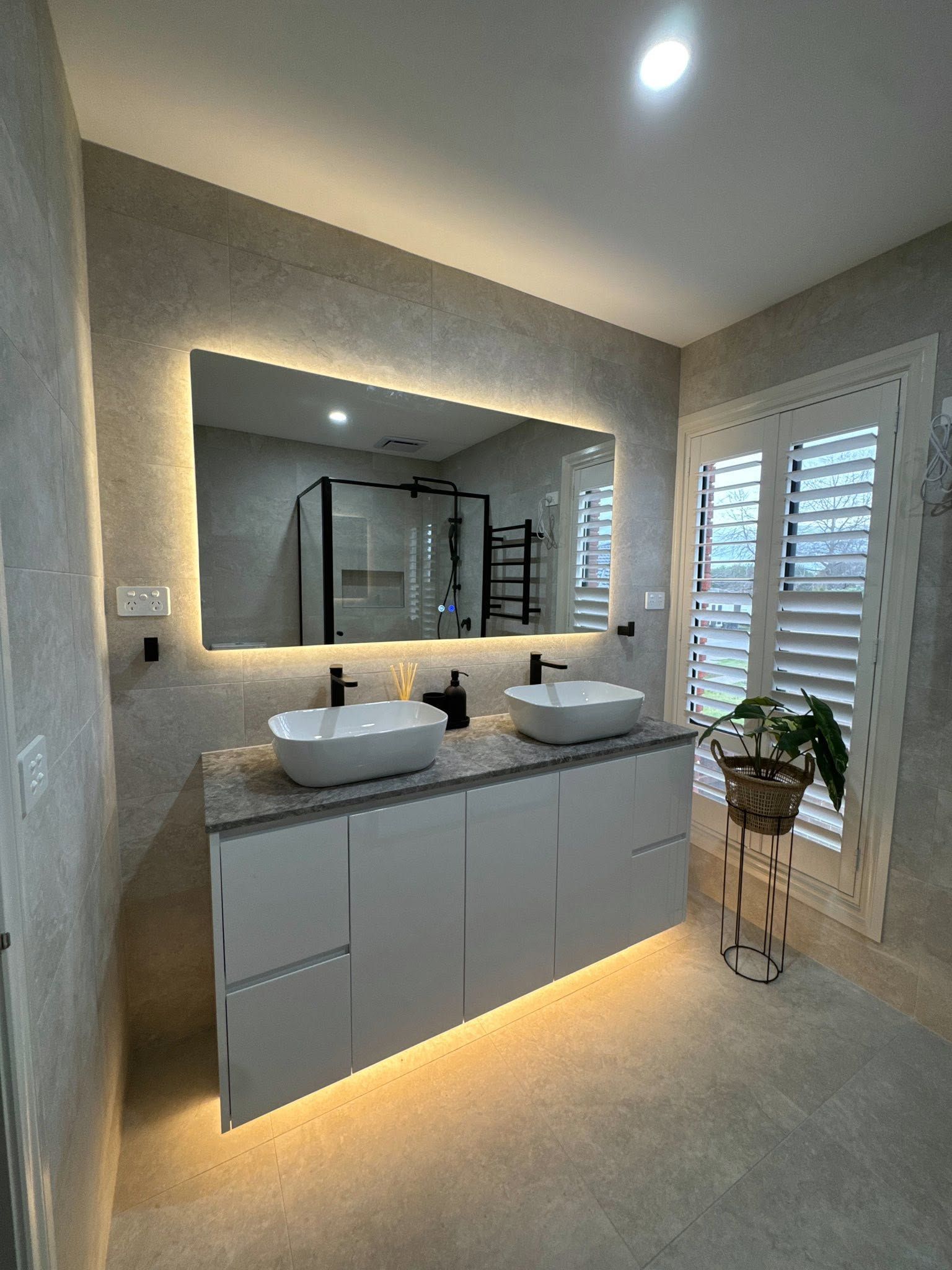 Modern bathroom with double vanity, backlit mirror, and warm under-cabinet lighting