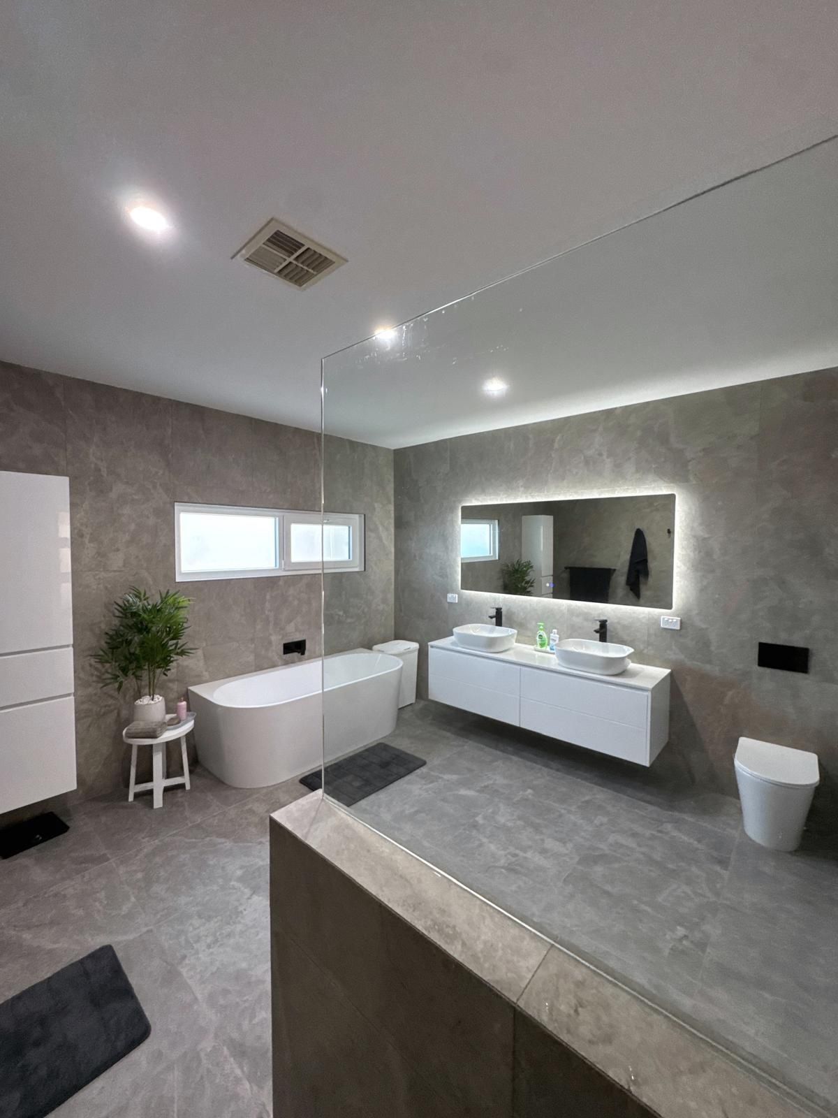 Modern bathroom with double sinks, round mirrors, and a light-tiled wall.