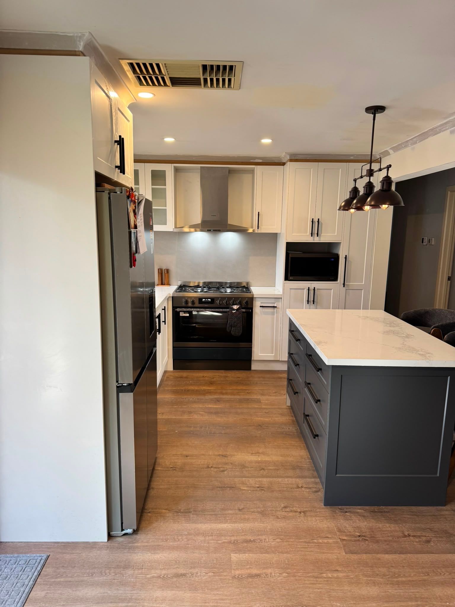 Bright modern white kitchen with large island, bar stools, stainless appliances, and pendant lights