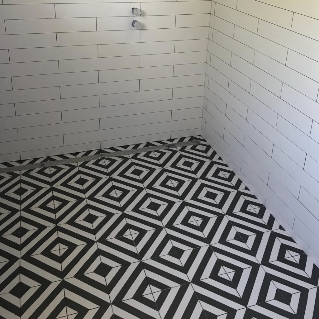 Empty tiled bathroom corner with black-and-white geometric floor and white tiled walls.