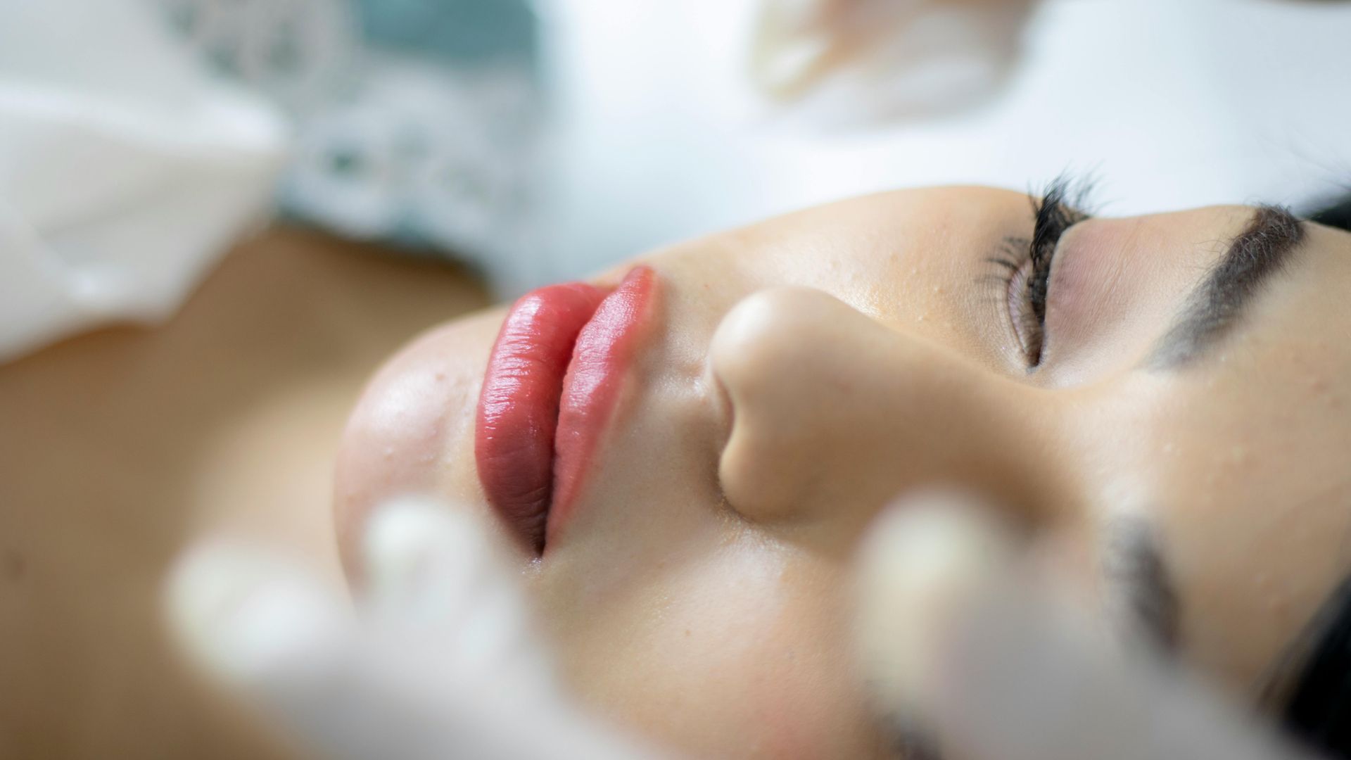 Primer plano de una persona tumbada en una camilla de spa con los ojos cerrados y pintalabios rojo, en actitud relajada.