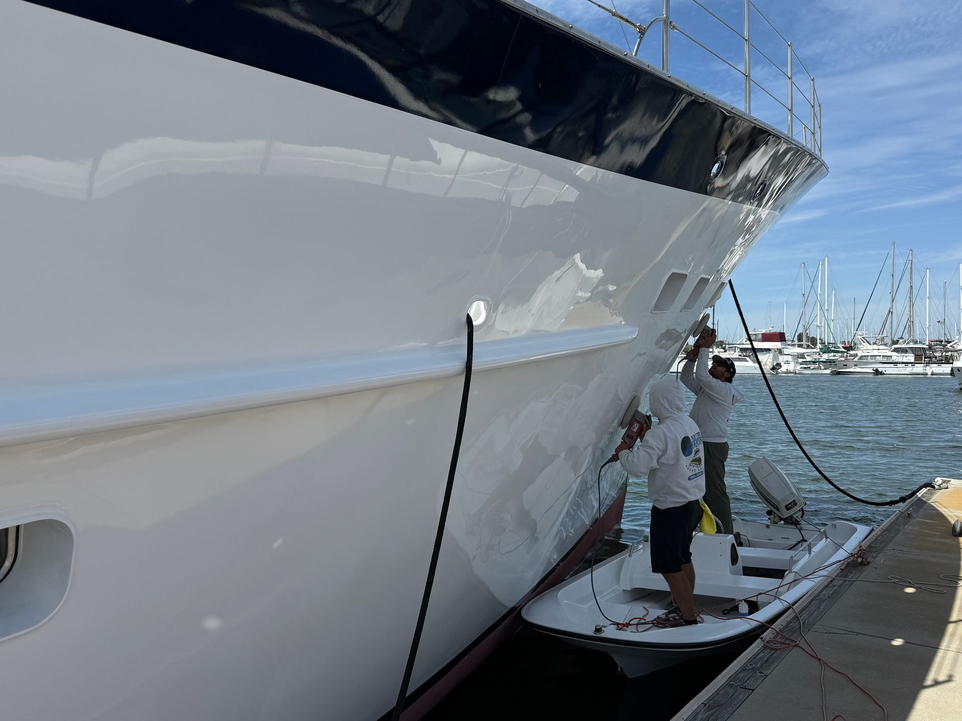 Person on a dock washing a large white yacht beside a marina.