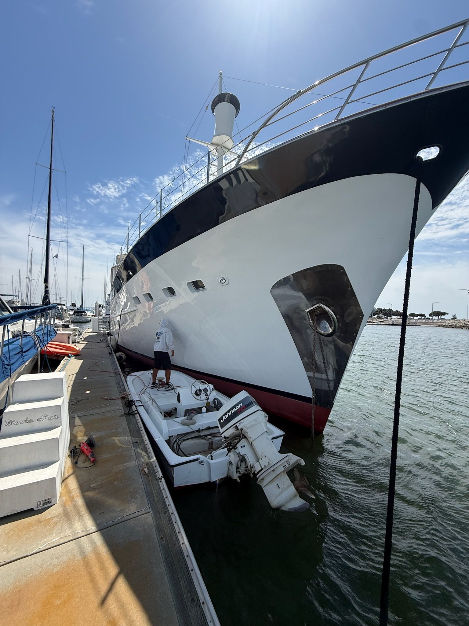 Large white yacht docked beside a pier on a sunny day, with a blue sky and calm harbor water.