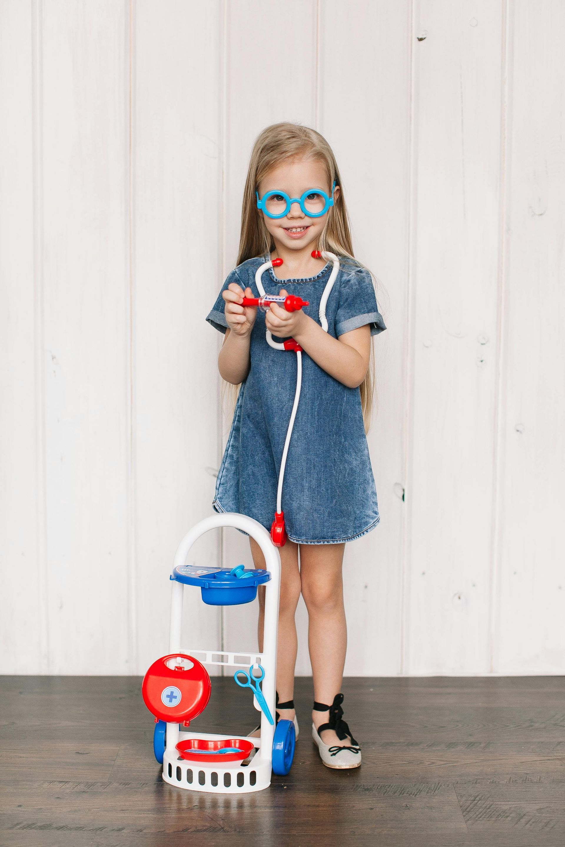 Young girl dressed up as a doctor. She is smiling and has medical-looking toys. 