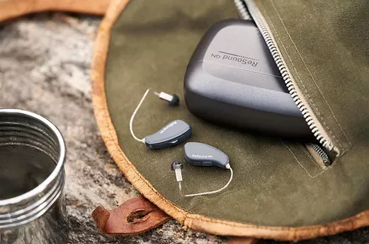 Hearing aids and charging case in a canvas pouch, outdoors.
