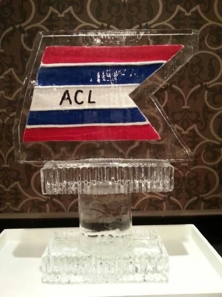 ACL logo plaque on a clear glass stand against a dark patterned background