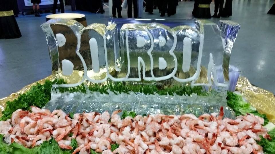 Ice sculpture spelling “BURBUNY” on a table, surrounded by shrimp and green garnish at an event