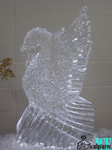 Transparent glass bird sculpture with raised wing on a tiled background