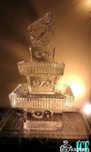 Clear ice sculpture of stacked bowls or baskets lit by warm amber lights on a table
