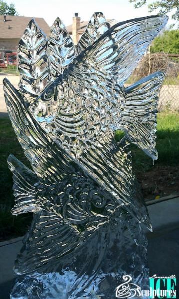 Shimmering glass sculpture of an abstract fish or bird, with metallic blue and silver highlights outdoors