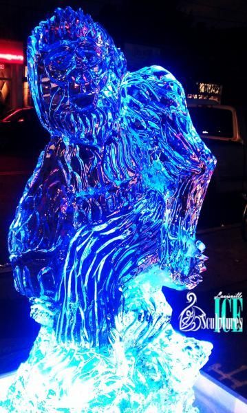 Glowing blue illuminated gorilla sculpture at night, with bright white light at the base and dark background