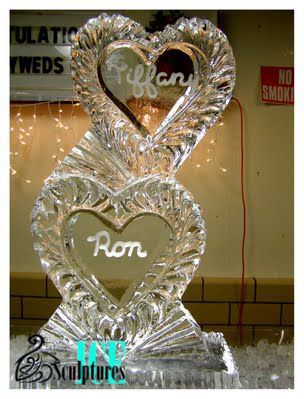 Heart-shaped ice sculpture with two carved hearts and names, displayed indoors at an event.