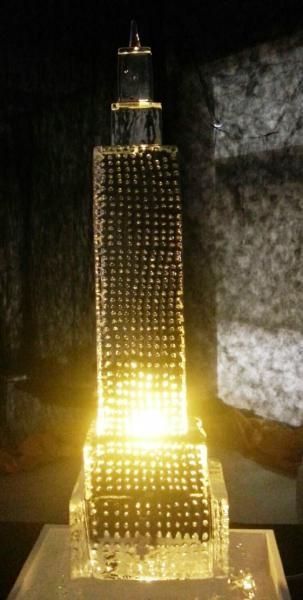 Lit miniature model of a tall skyscraper with bright lights at the base against a dark background