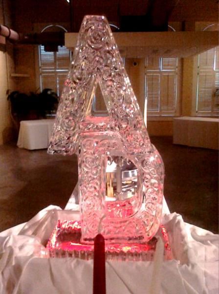 Ice sculpture of a large letter A glowing pink on a table indoors.