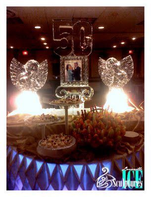 Decorated 50th anniversary dessert table with photo centerpiece, glowing wing decorations, and flowers