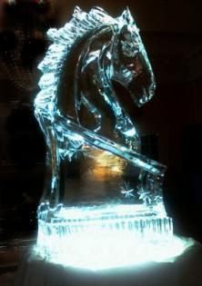 Ice sculpture of a horse illuminated with blue-white light on a dark background