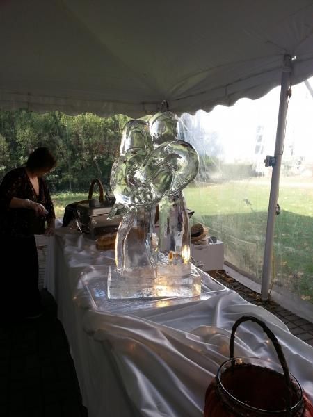 Ice sculpture on a table under a white event tent, with a person working nearby.