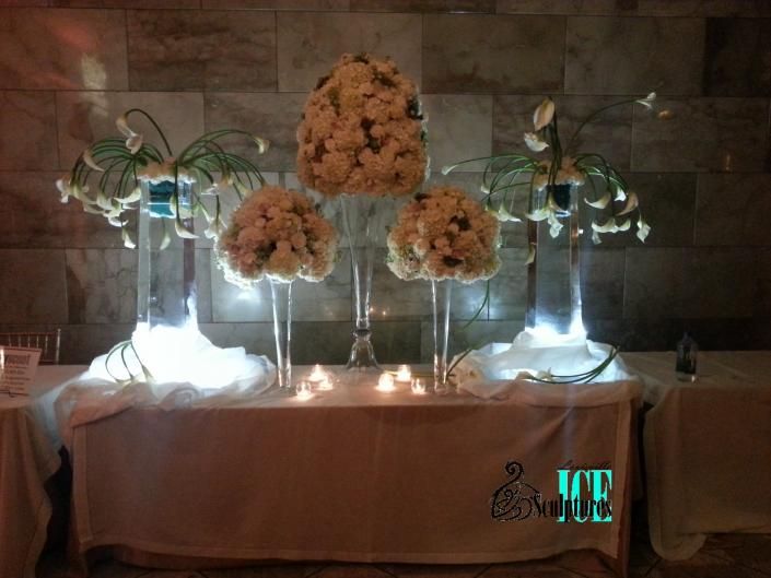 Glowing floral wedding table display with white and peach arrangements on a draped table against a stone wall