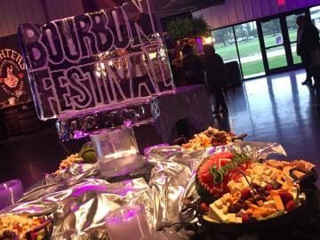 Buffet table with trays of food at a Bourbon Festival indoors, with purple lighting and a banner in the background