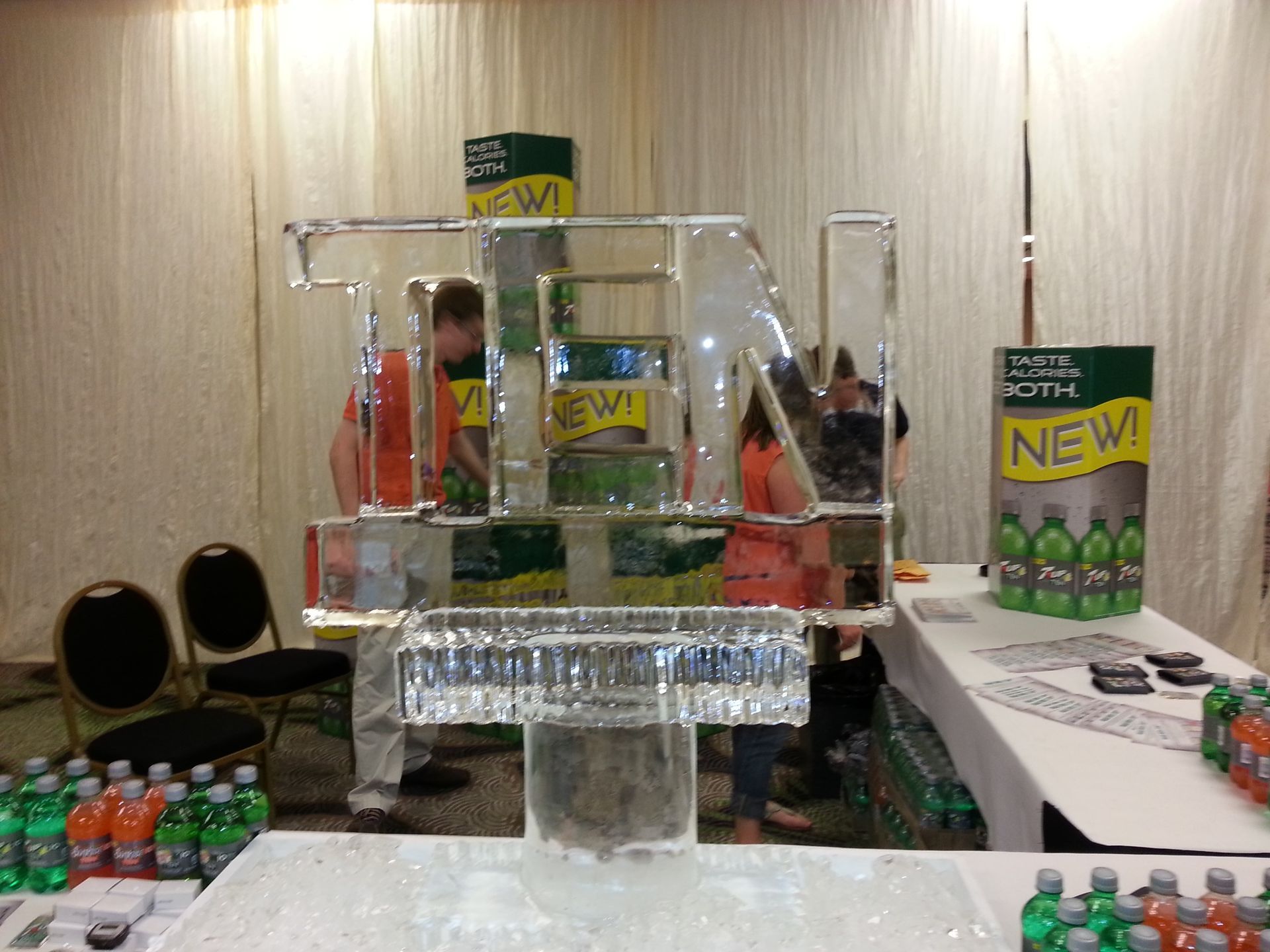 Promotional display with clear acrylic shelves holding colorful canned drinks on a trade show table