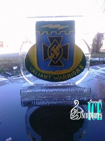 Blue and green “Valiant Warriors” crest on a clear display against a bright outdoor background