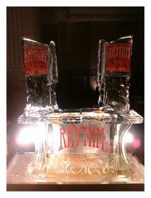 Clear ice sculpture with red “RHYTHM” lettering, lit from below against a dark background.