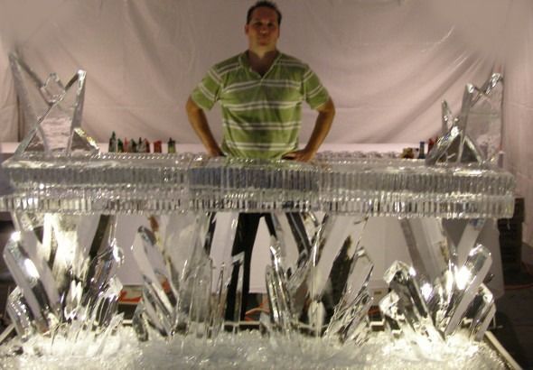 Man standing behind a bar covered in silver foil and ice-like decorations under a draped white backdrop