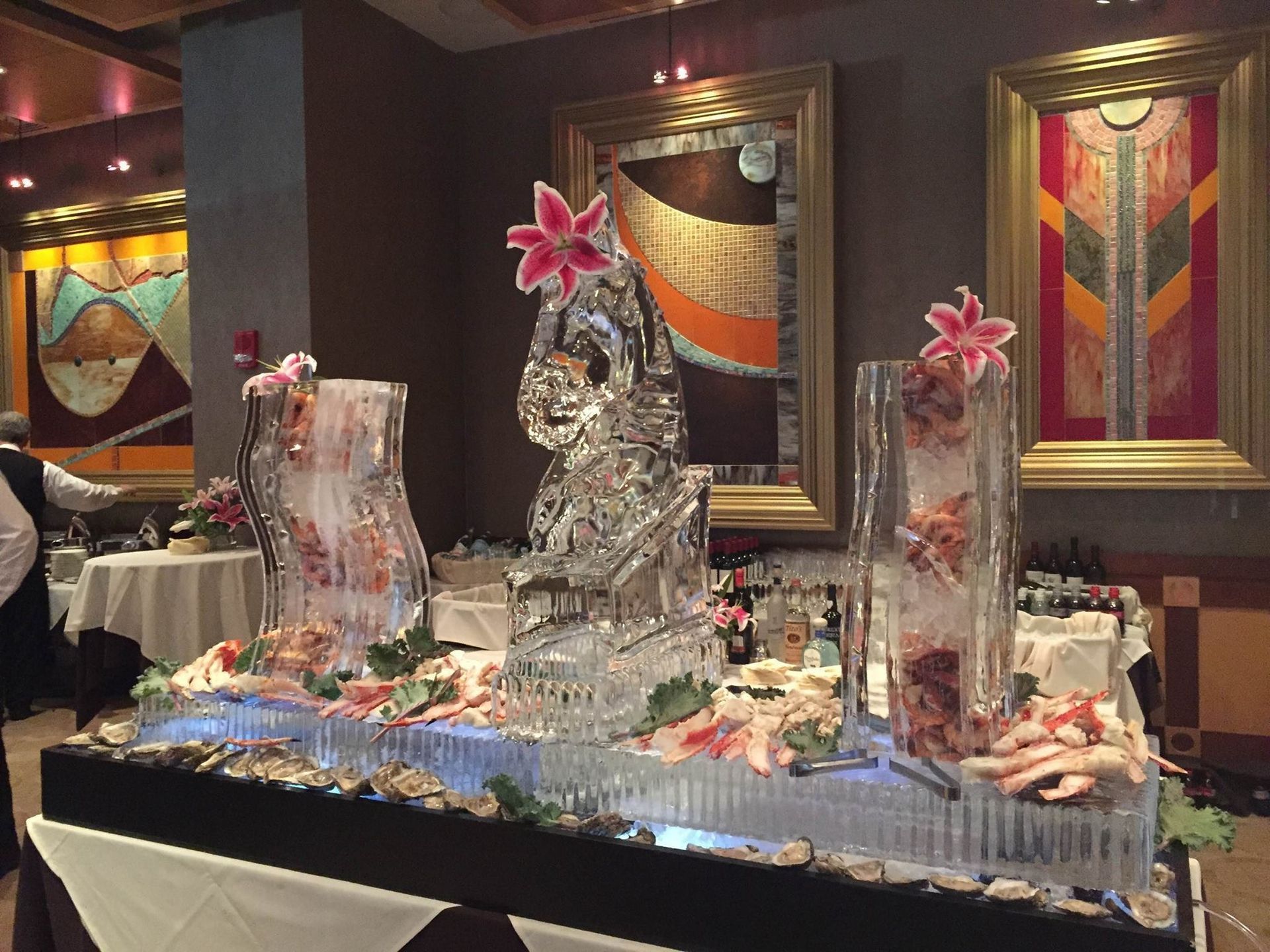 Ice sculpture centerpiece on a banquet table in a warmly lit dining room, decorated with pink flowers.