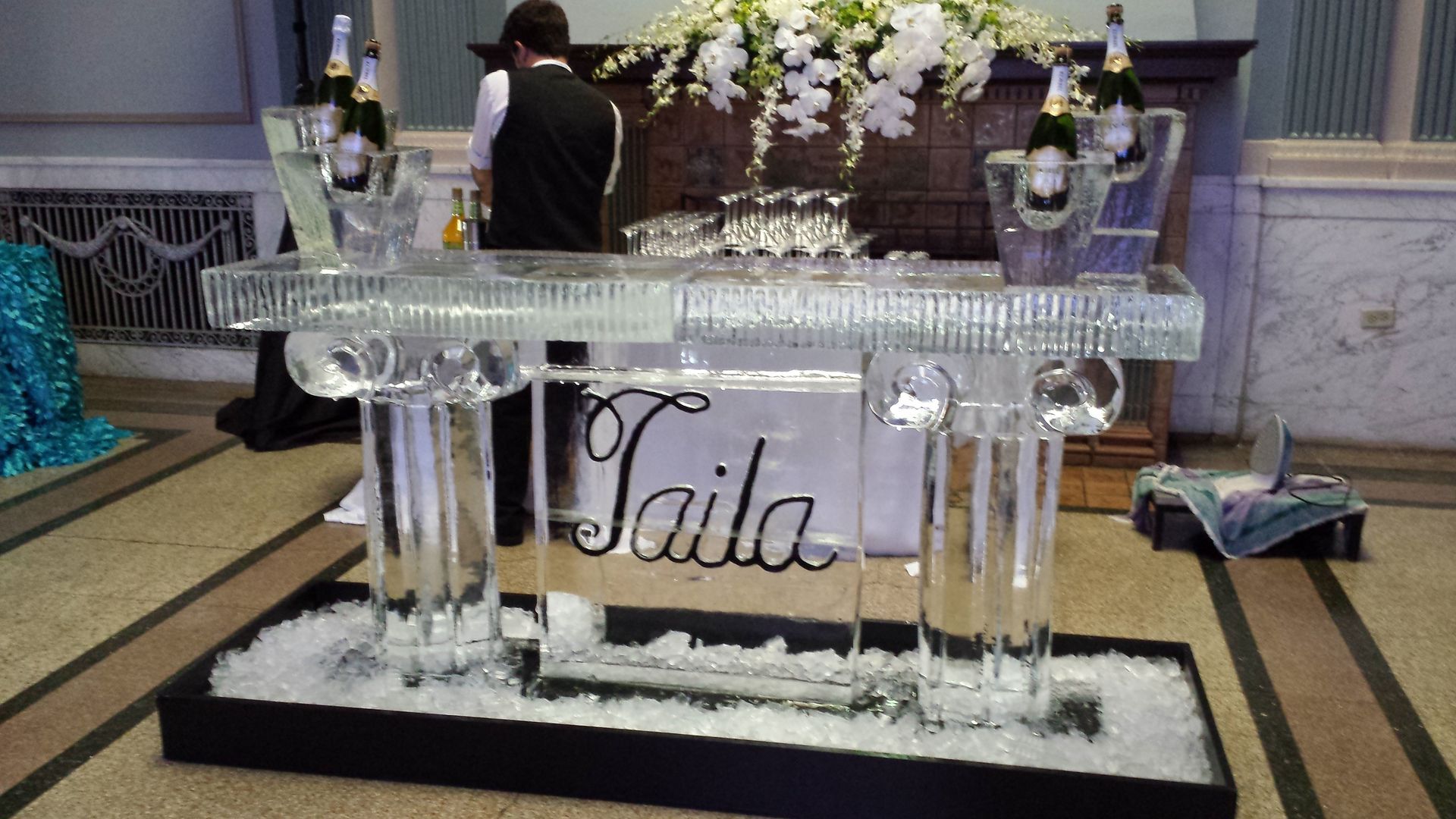 Crystal banquet table display with tall vases and the name “Gaila” in front, at an event hall