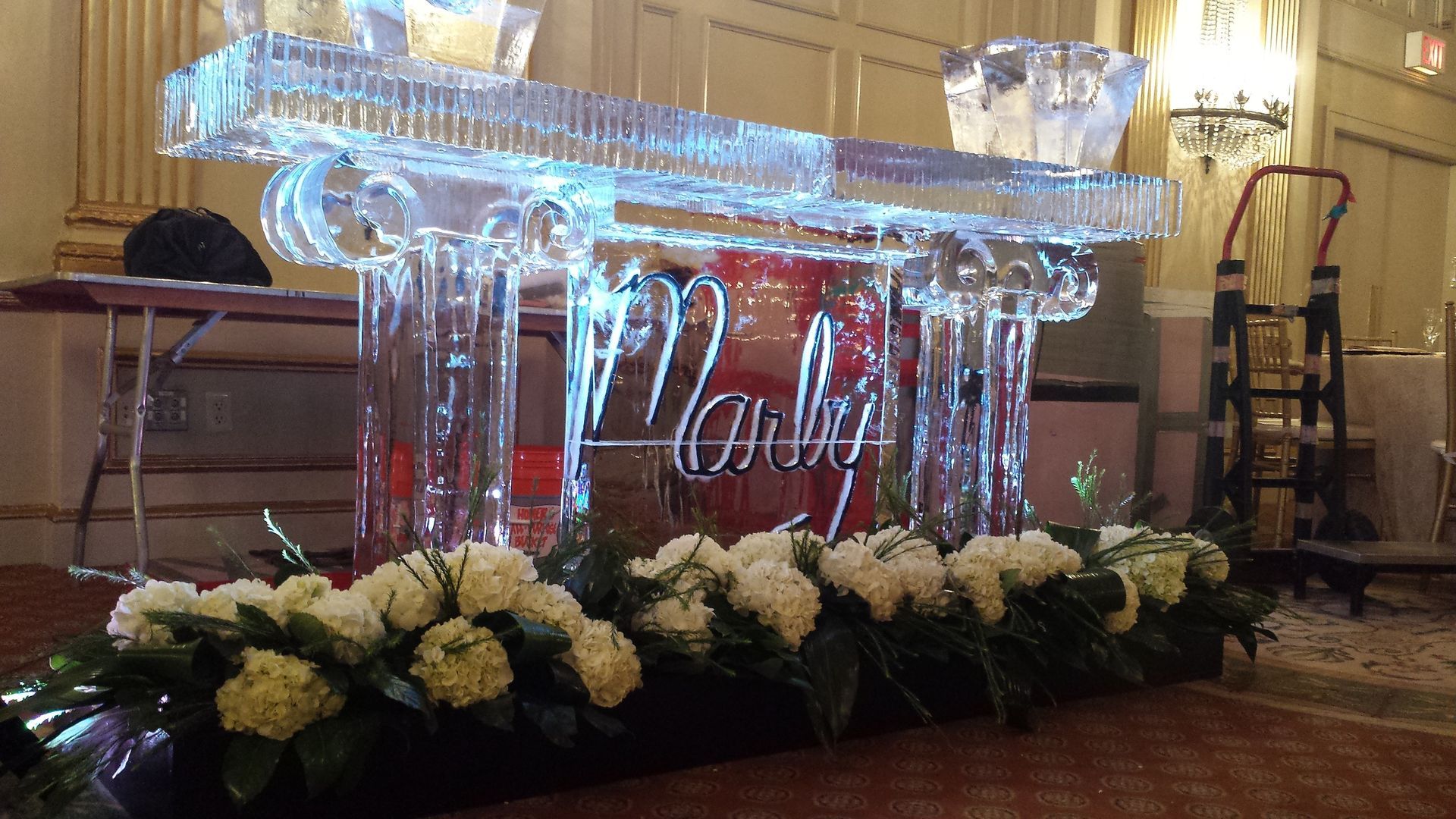 Illuminated clear crystal stage with white flowers and red “Happy” sign at a banquet event